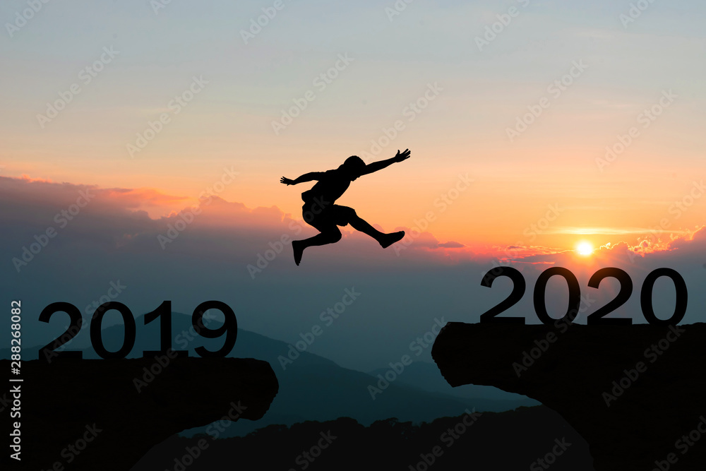 Happy New Year 2020 Men jump over silhouette mountains sun