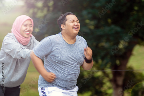 two people, with young Muslim women encouraging Asian male friends who are overweight to exercise that is running