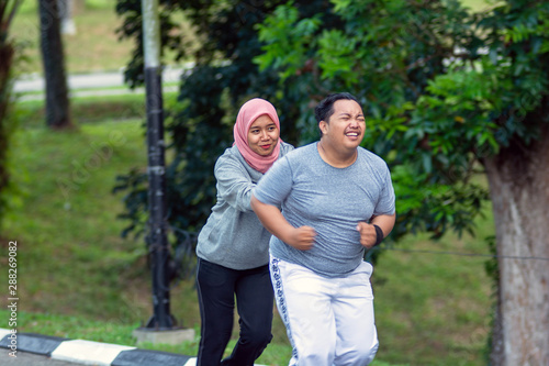 two people, with young Muslim women encouraging Asian male friends who are overweight to exercise that is running © SVRSLYIMAGES