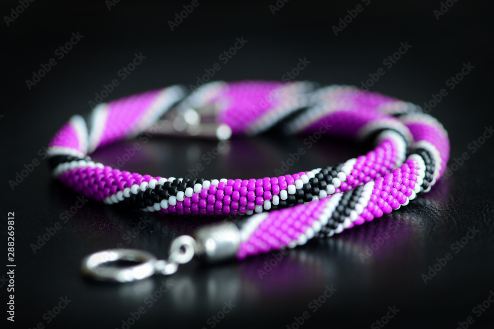 Beaded necklace purple, black and white colors on a dark background close up Beaded necklace purple, black and white colors on a dark background close up