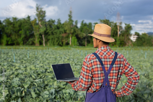 Agriculture man holding a notebook standing at his garden with modern agricultural concepts.