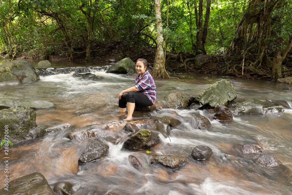 Asian women be smile sitting relaxing and enjoying view in waterfall in greens jungle. Traveling along mountains and rain forest, freedom and active lifestyle concept. Asia, Thailand