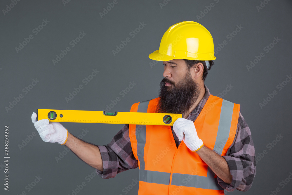 An engineering man wearing a yellow helmet holding a water level meter on a gray background. An engineering man wearing a yellow helmet holding a water level meter on a gray background.