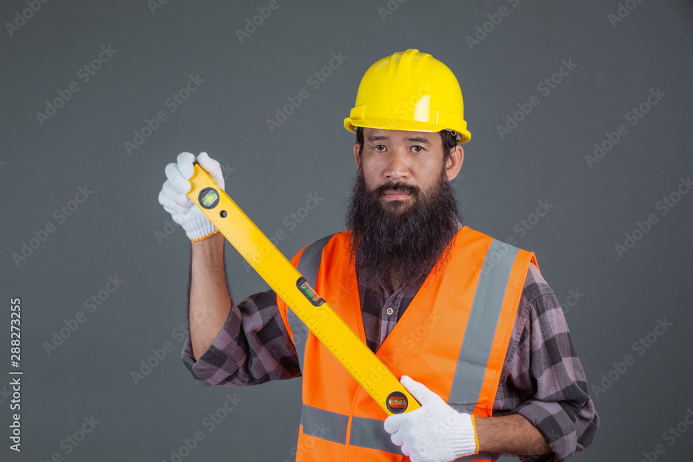 An engineering man wearing a yellow helmet holding a water level meter on a gray background. An engineering man wearing a yellow helmet holding a water level meter on a gray background.