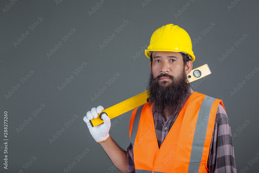 An engineering man wearing a yellow helmet holding a water level meter on a gray background. An engineering man wearing a yellow helmet holding a water level meter on a gray background.