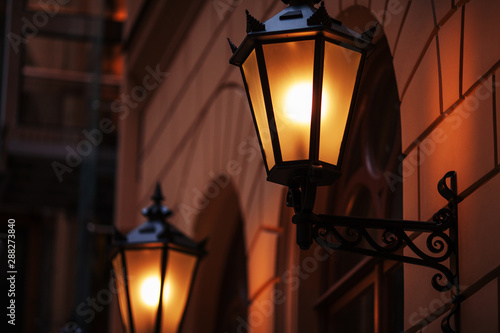 Old fashioned street lamp at night. Brightly lit street lamps at sunset. Decorative lamps. Magic lamp with a warm yellow light in the city twilight © fadzeyeva