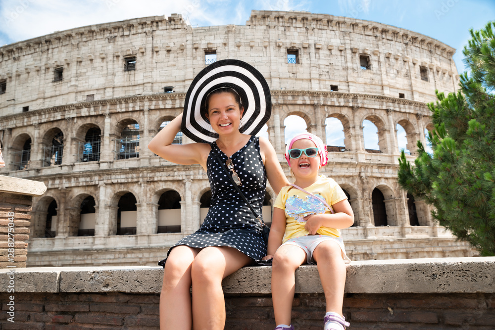 Young Mother And Daughter Sitting In Front Of Colosseum