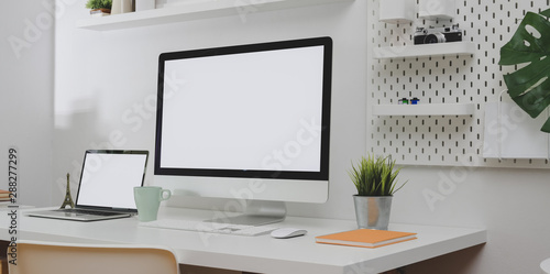 Desktop computer and blank screen laptop with copy space and office decorations in minimal white office room