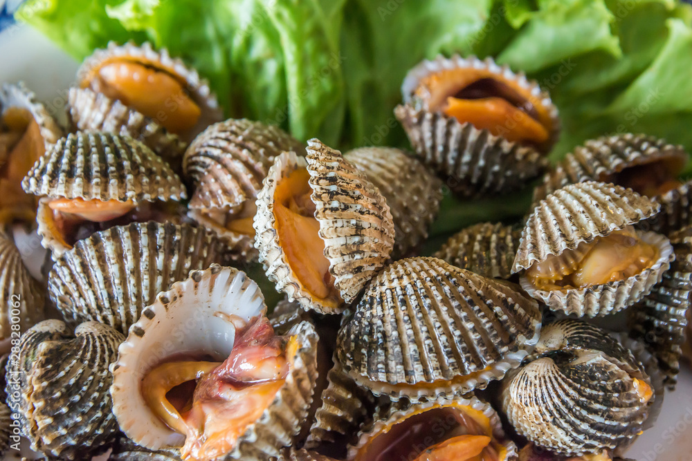 Steamed blanched cockles with Thai seafood dipping sauce and lettuce in the white dish.