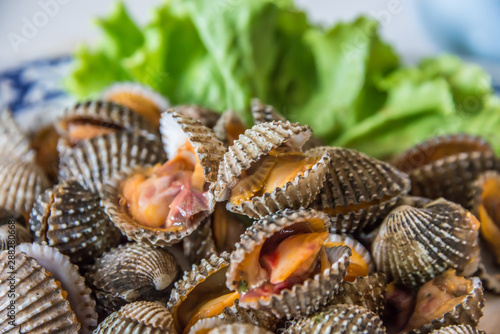 Steamed blanched cockles with Thai seafood dipping sauce and lettuce in the white dish.