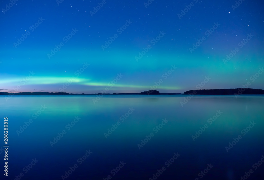 Fototapeta premium Northern lights dancing over calm lake in Farnebofjarden national park in Sweden.