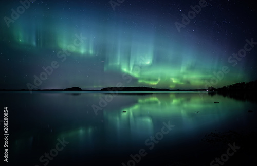Northern lights dancing over calm lake in Farnebofjarden national park in Sweden.