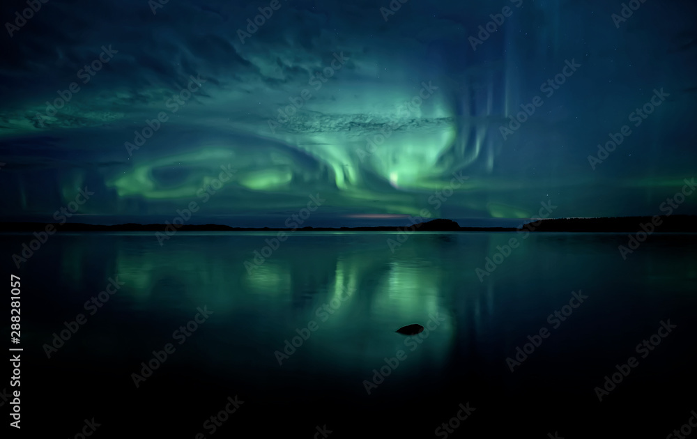 Northern lights dancing over calm lake in Farnebofjarden national park in Sweden.