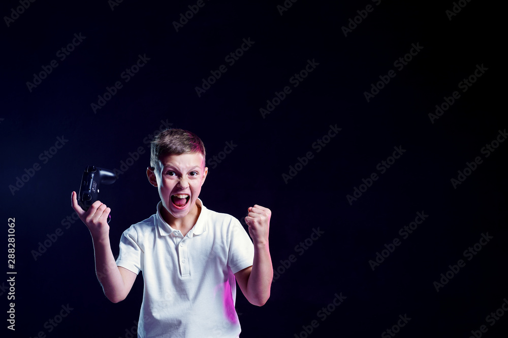Naklejka premium Cheerful kid with open mouth and joystick shouting for joy after winning in video game on black background