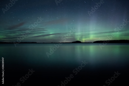 Northern lights dancing over calm lake in Farnebofjarden national park in Sweden.