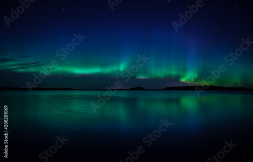 Northern lights dancing over calm lake in Farnebofjarden national park in Sweden.