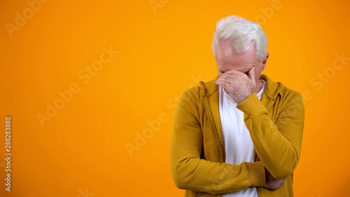 Dissatisfied retired man closing face with palm, failure concept, disappointment