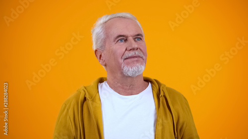 Thoughtful elderly male looking up, dreaming of good things, yellow background © motortion