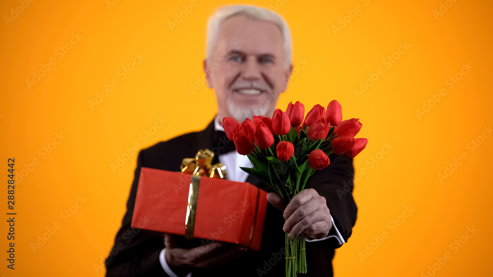 Smiling aged man in suit presenting tulips bouquet and giftbox, sincere greeting Smiling aged man in suit presenting tulips bouquet and giftbox, sincere greeting