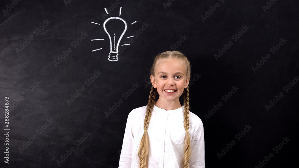 Schoolgirl smiling at camera, light bulb painted on blackboard, found answer