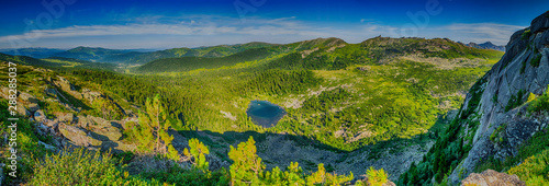 Panoramic view from the cliff on beautifull valley with small mountain lake  green forest and sayan mountain range in Ergaki nature park in Krasnoyarsk region  Russia