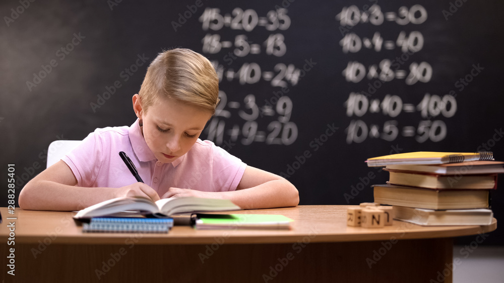 Schoolboy doing sums on math lesson, sitting against blackboard, knowledge Schoolboy doing sums on math lesson, sitting against blackboard, knowledge