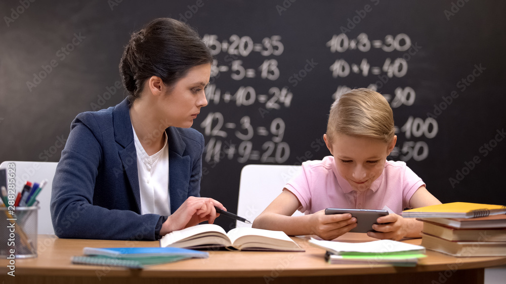 Unhappy teacher trying to explain task to boy playing on smartphone, disrespect Unhappy teacher trying to explain task to boy playing on smartphone, disrespect