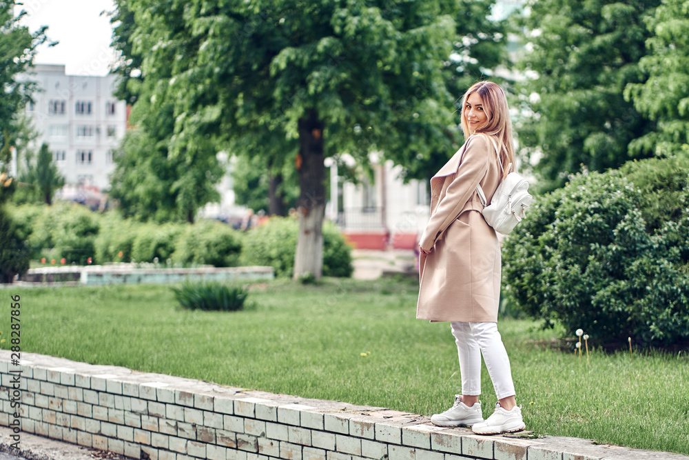 Fototapeta premium girl in a brown coat and white jeans. walking around the city