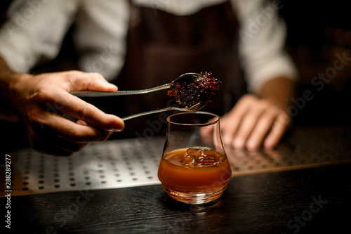 Bartender adding chilled melting caramel with twezzers to the cocktail glass with ice cubes photo