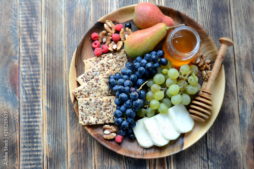 Wine snacks on a wooden platter: cheese, nuts, crackers, pears