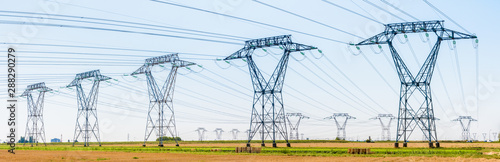 фотографія Panoramic view of a row of electricity pylons in the countryside with dozens of other pylons in the distance