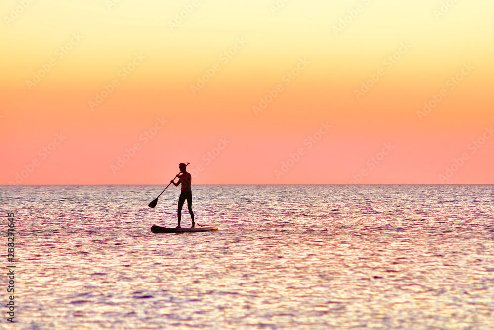 Paddle boarding at sunset. Silhouette of sup surf swimmer on a quiet sea.