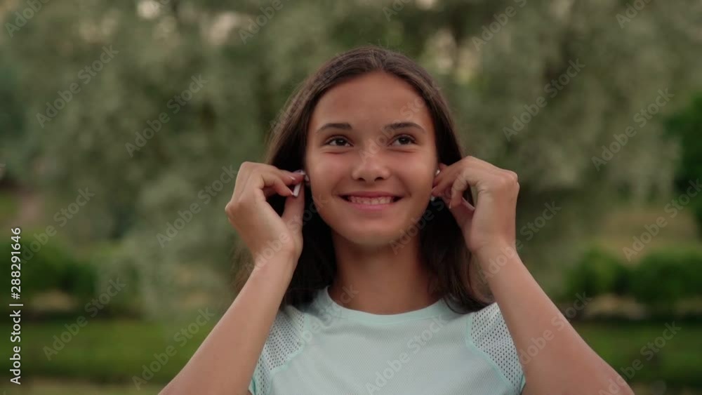 smiling girl teenager in white t-shirt puts on headphones and straightens long loose flowing hair closeup slow motion smiling girl teenager in white t-shirt puts on headphones and straightens long loose flowing hair closeup slow motion