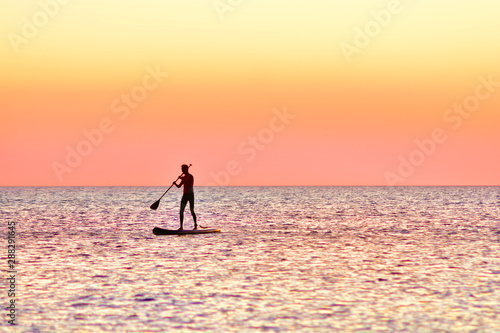 Paddle boarding at sunset. Silhouette of sup surf swimmer on a quiet sea.