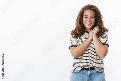 Lovely kind tender curly-haired young chubby girl press palms together express cuteness touched moving gift smiling delighted receive present look surprised happy grinning white teeth