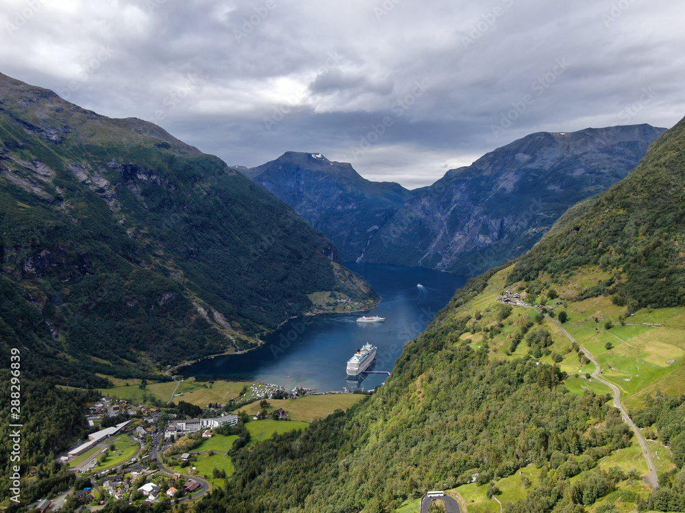 Geiranger (Norway) Der Wunderschöne Geiranger Fjord in Norwegen ,  Drohnen Foto ,mit See und Sicht auf Felsen bei blauem Himmel mit kleinen Norwegischen Häusern , Beauty of Norway	