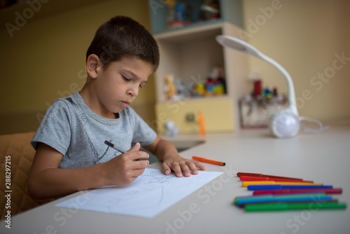little boy draws with colored pencils