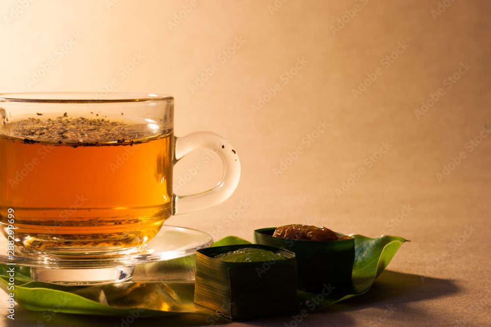 Thai sweets in banana leaves and cup of tea that are arranged on leaf with brown paper background. Thai sweets in banana leaves and cup of tea that are arranged on leaf with brown paper background.