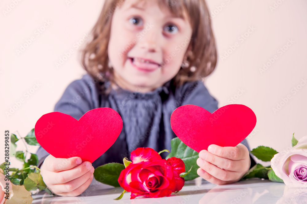 Humorous photo of little sweet child girl with flowers holding two red hearts. Wedding, Valentine, love concept. Humorous photo of little sweet child girl with flowers holding two red hearts. Wedding, Valentine, love concept.