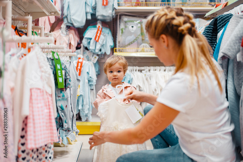 Mother with girl choosing clothes in kids store