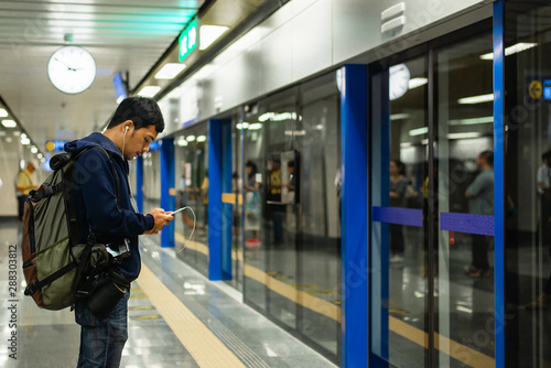 Exterior of moder Bangkok metro with passengers on seats and young man using their cell phones. Corporate business people commuting to work by public transport. Horizontal composition.