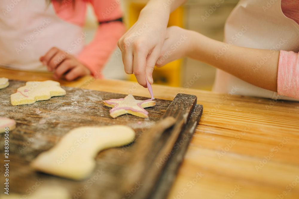 Little girls cooks cover cookies with sweet layer