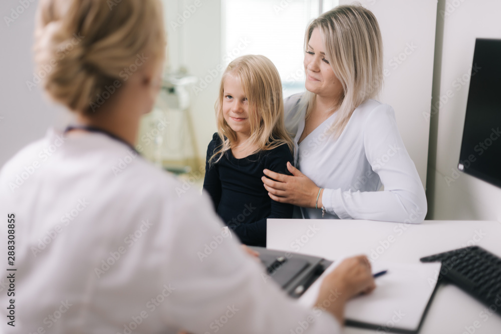 Pediatrician doctor examining cute kid girl with blond hair . Mother holding baby in her hands.