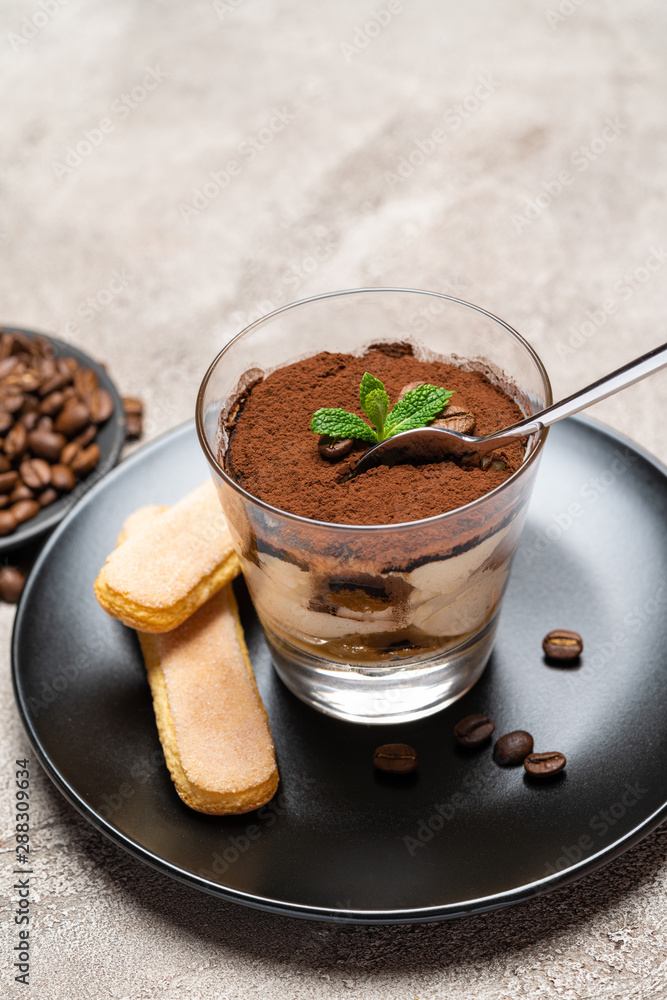Portion of Classic tiramisu dessert in a glass cup on concrete background Portion of Classic tiramisu dessert in a glass cup on concrete background