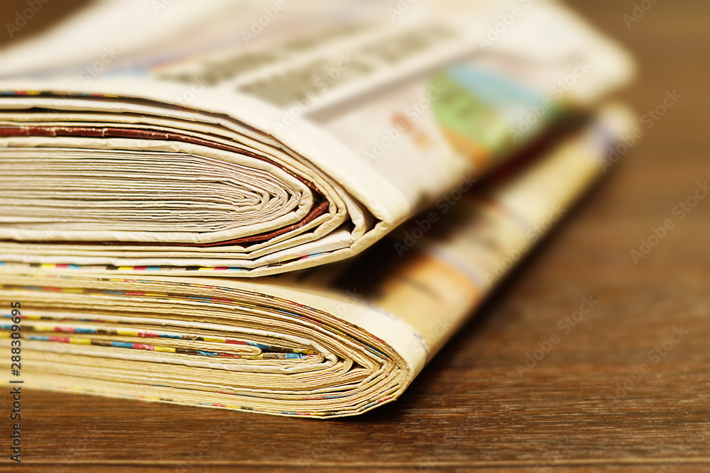 Lots of newspapers folded and stacked in one pile. Stack of old journals concept for communication. Pages with news on wooden table for background. Side view, selective focus Lots of newspapers folded and stacked in one pile. Stack of old journals concept for communication. Pages with news on wooden table for background. Side view, selective focus