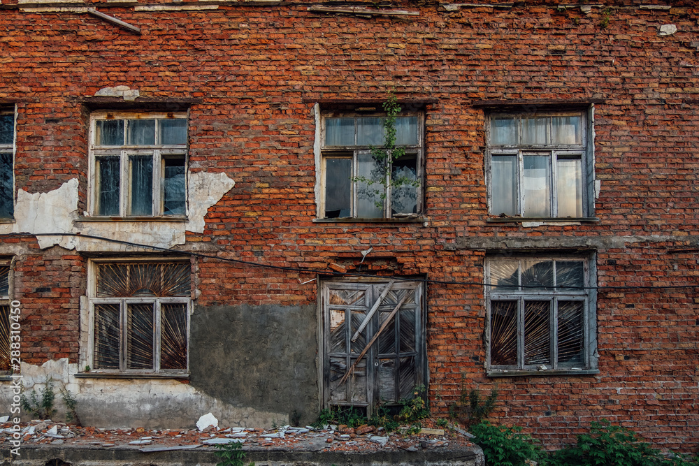 Old grungy wall of red brick with broken windows and wooden door