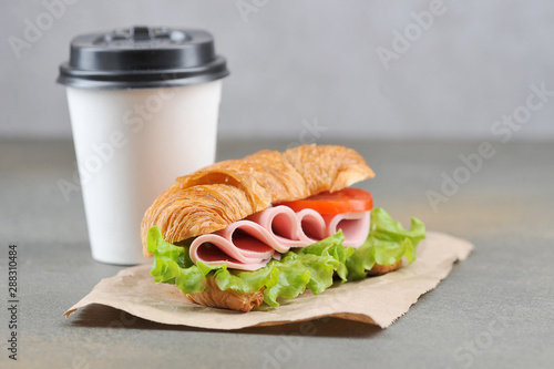Coffee paper cup and ham sandwich. The concept of fast food and coffee to go. Gray background. Close-up.