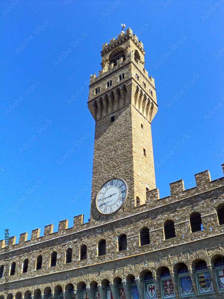 Palazzo Vecchio at piazza Della Signoria, Florence Italy. Famous historical building with bell tower with clock on blue sky background. Currently old Palace serves as a town hall.