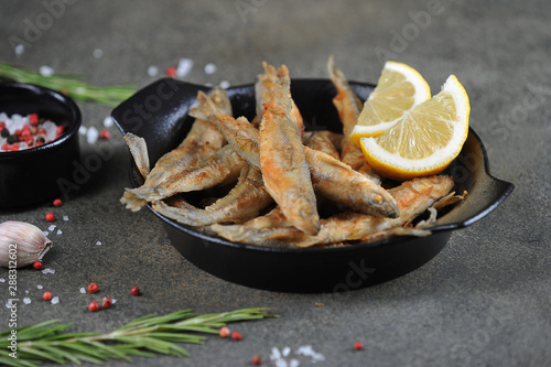 фотографія Fried smelt fish with lemon slices in a black pan