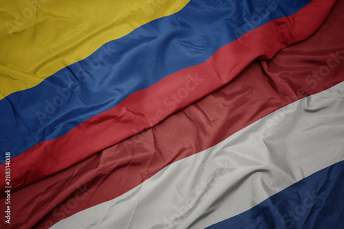 waving colorful flag of netherlands and national flag of colombia.